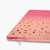 Close-up of gold foil notes and ideas text on pink ombre notebook