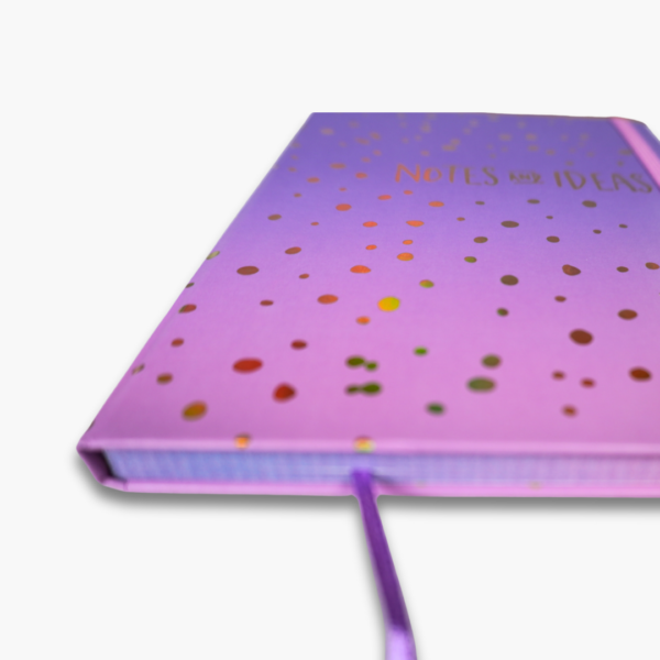 Close-up of gold foil notes and ideas text on purple pink ombre notebook