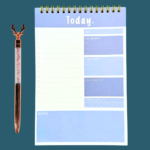 Blue A5 daily planner notepad ring-bound with sections for date, top 3 priorities, don’t forget, gratitude, water intake, to-do, and notes